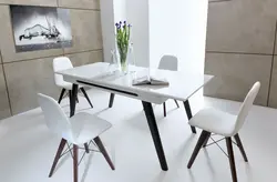 Мизи сафед ва курсиҳои сиёҳ барои акси ошхона