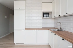 White Kitchen With Wooden Countertop And Black Handles In The Interior