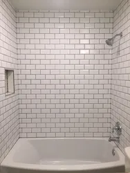 Bathtub with white tiles and gray grout photo